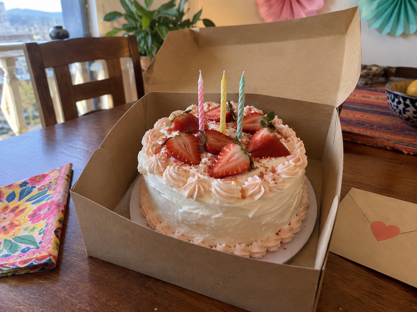 Small strawberry tres leches birthday cake with candles in a bakery box